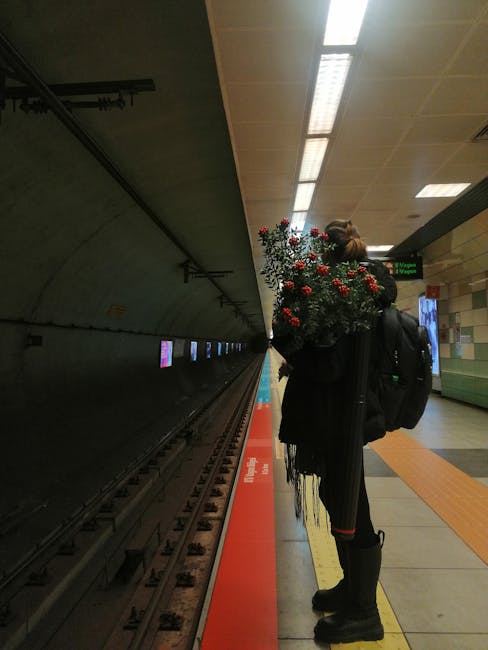 A woman standing on a Dagenham Heathway station platform holding a large bouquet of fresh flowers. The bouquet features a mix of red, white, and green blooms, with roses and smaller filler flowers arr